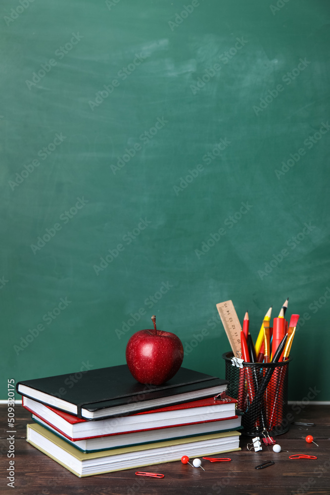 School stationery with books and apple on table near green chalkboard School stationery with books and apple on table near green chalkboard
