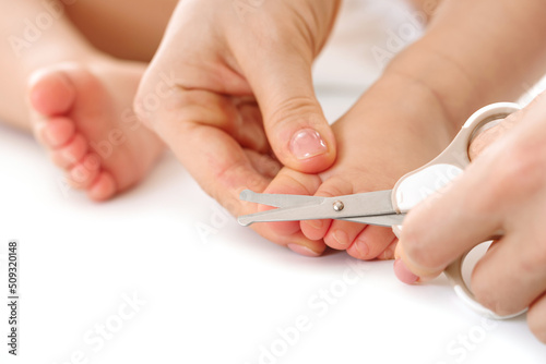 Mother holding little child's foot and cutting toenails.