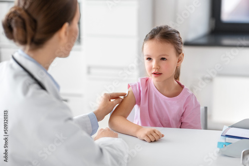 medicine, healthcare and vaccination concept - female doctor or pediatrician disinfecting arm skin of little girl patient at clinic