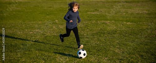 Soccer kid boy playing football. Child boy play football on outdoor field. Children score goal at soccer game. Young boy kicks the soccer ball. Football player in motion, boy in movement, banner. © Volodymyr