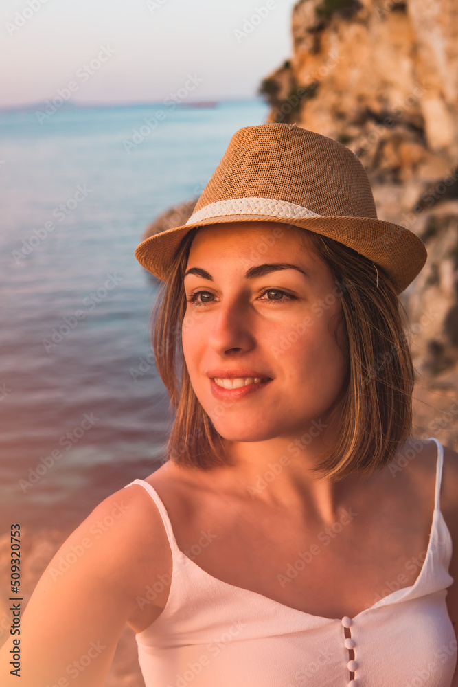Portrait, smiling young woman on holiday, looking at the landscape at sunset in the cove of Portal Vells, island of Palma de Mallorca, Spain.