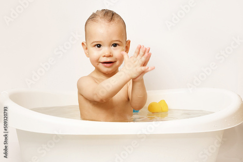 Smiling little boy taking a bath with rubber toys.