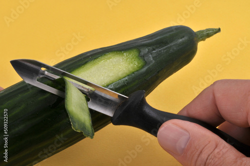 Préparation d'un concombre avec un épluche légume en gros plan sur fond jaune photo