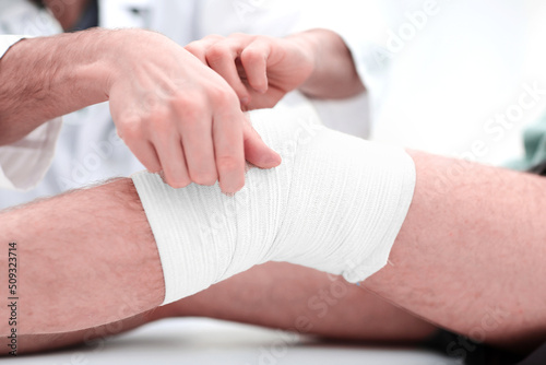 Mid section of doctor bandaging leg of patient in hospital