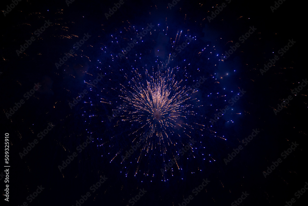 A bright firework with an orange glowing center and blue sparks to the side against the background of the night sky. High quality photo A bright firework with an orange glowing center and blue sparks to the side against the background of the night sky. High quality photo
