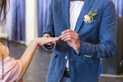 bride and groom. wedding ring and wedding bouquet. spring summer celebration. he puts a ring on her hand. blue wedding suit. purple bouquet and gold rings.
