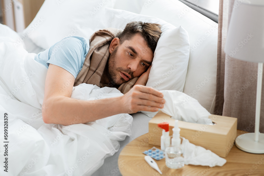 people and health problem concept - unhappy sick man lying in bed at home and taking paper tissue from box people and health problem concept - unhappy sick man lying in bed at home and taking paper tissue from box