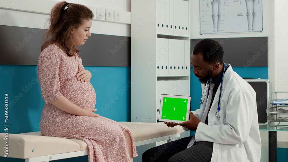 Pregnant patient and doctor analyzing horizontal greenscreen on digital tablet. Obstetrician using blank copyspace with mockup template and isolated chroma key background. Tripod shot. Pregnant patient and doctor analyzing horizontal greenscreen on digital tablet. Obstetrician using blank copyspace with mockup template and isolated chroma key background. Tripod shot.