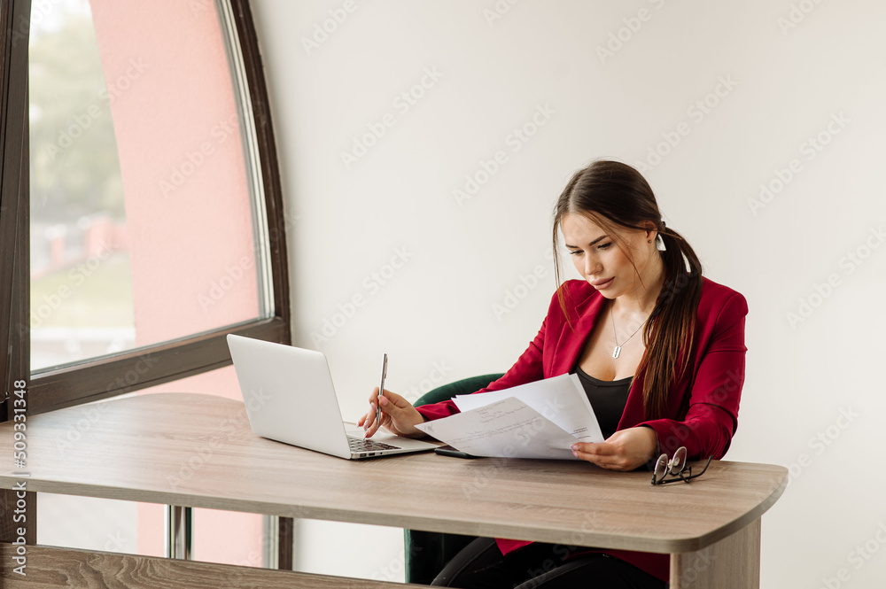Successful business woman dressed in red jacket is working with a laptop in the office Successful business woman dressed in red jacket is working with a laptop in the office