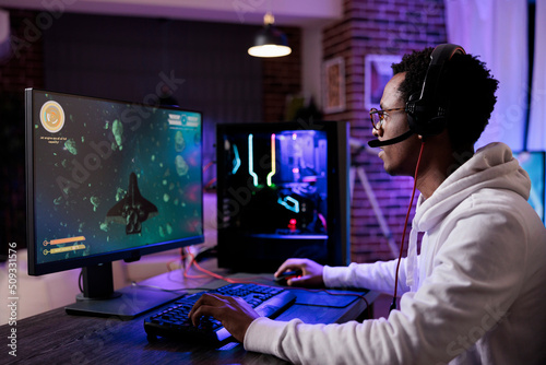 Young gamer playing online shooting video games, streaming action rpg competition on pc with neon lights. Male streamer having fun with esport gaming championship on computer. photo