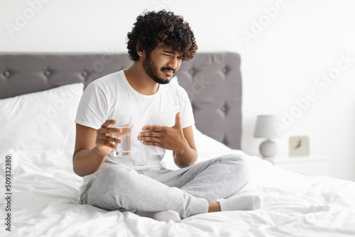 Eastern man suffering from heartburn, sitting on bed photo