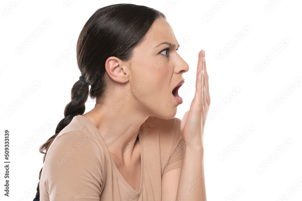 Profile of a young frowning woman checks her breath with her palm on a white background Profile of a young frowning woman checks her breath with her palm on a white background