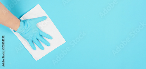 Top view.Hand is wiping and hold white paper tissue on blue background. Hnad wear blue nitrile disposable glove .Empty space for text . photo