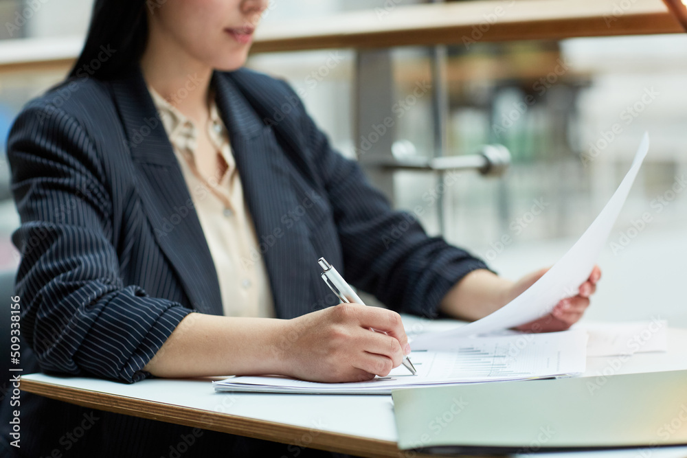 Close up of young businesswoman writing in document while working at cafe table in office building setting, copy space Close up of young businesswoman writing in document while working at cafe table in office building setting, copy space