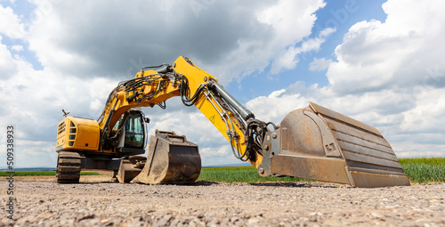 Yellow Excavator at Construction Site. Excavating machinery at the construction site on blue cloud sky background.