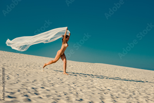 Beautiful nude mature woman running on sandy beach in summer