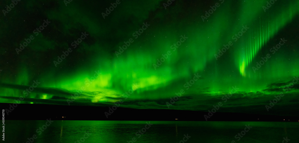 Amazing Northern lights over the plain lake with green reflections
