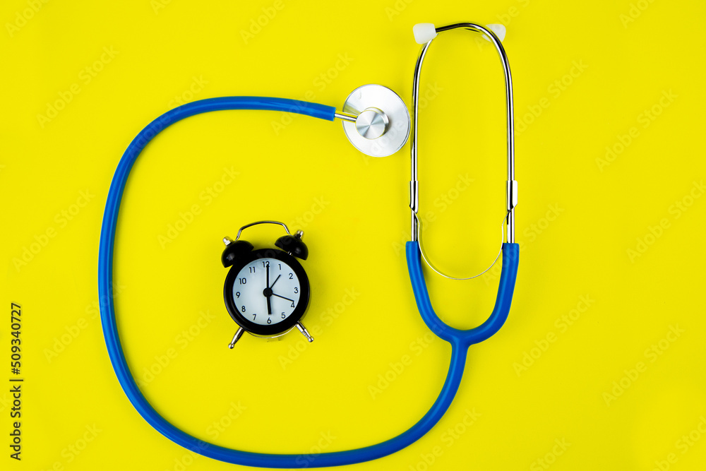 Black alarm clock lies inside a blue phonendoscope on a bright yellow background. High quality photo Black alarm clock lies inside a blue phonendoscope on a bright yellow background. High quality photo