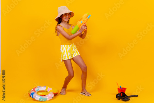Little girl playing with summer toys on a yellow background