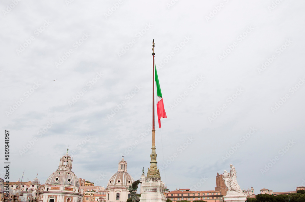 National flag of Italian republic il Tricolore waving on flagpole over ancient Rome cityscape