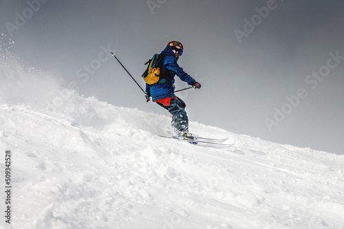Freeride, a man is stylishly skiing on a snowy slope with snow dust plume behind him