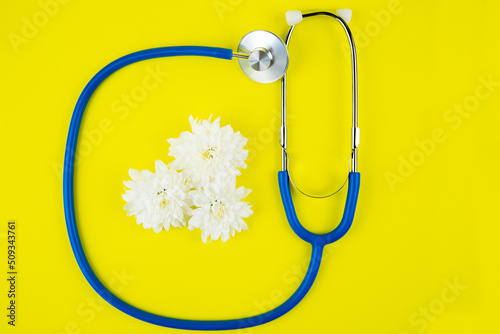 Blue phonendoscope lies on a bright yellow background with white flowers inside. High quality photo photo