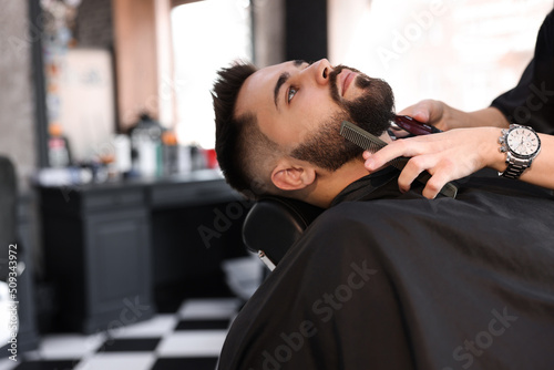 Professional hairdresser working with client in barbershop