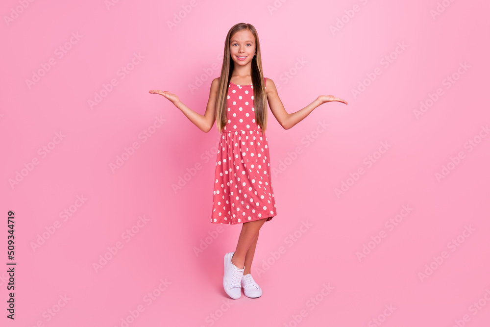 Full length portrait of little schoolgirl arms palms demonstrate empty space scales isolated on pink color background Full length portrait of little schoolgirl arms palms demonstrate empty space scales isolated on pink color background