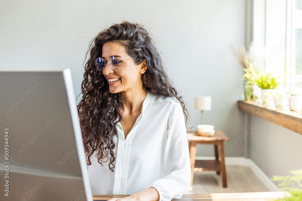 Portrait of young smiling woman looking at PC computer. Happy girl seating in creative office. Successful businesswoman. Modern business woman. Portrait of young smiling woman looking at PC computer. Happy girl seating in creative office. Successful businesswoman. Modern business woman.