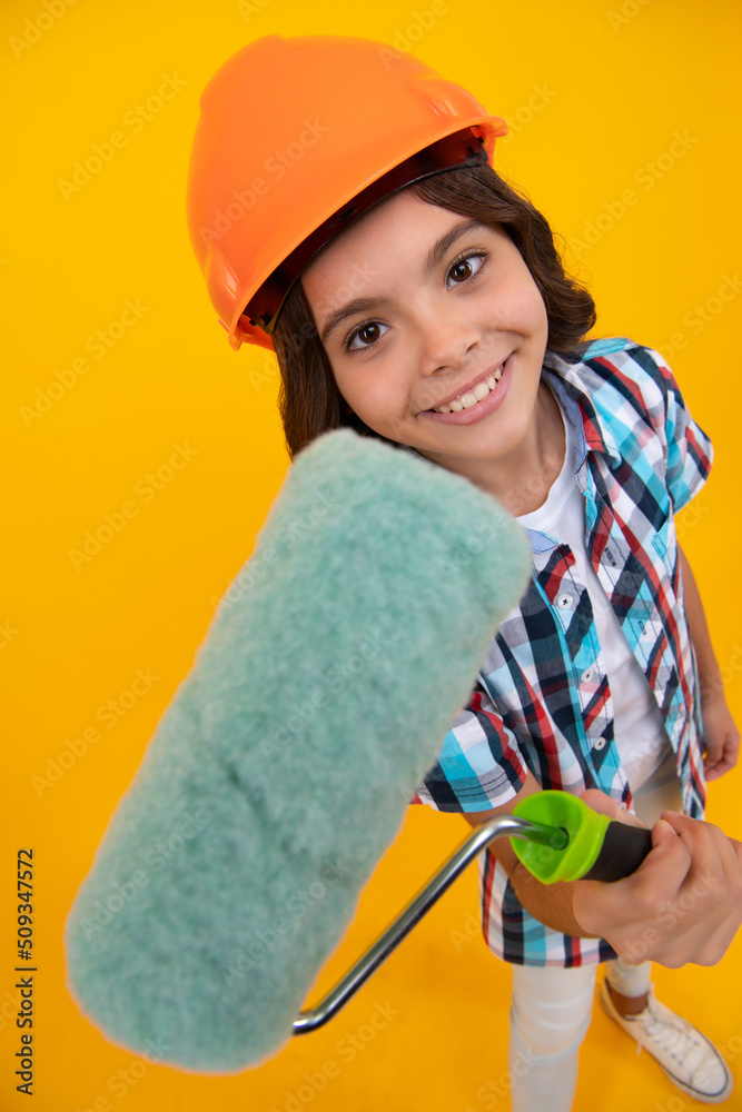 Painter in workshop. Renovation and repair. Teen girl in helmet with painting brush. Child in hard hat. Kid builder painter on construction site. Painter in workshop. Renovation and repair. Teen girl in helmet with painting brush. Child in hard hat. Kid builder painter on construction site.
