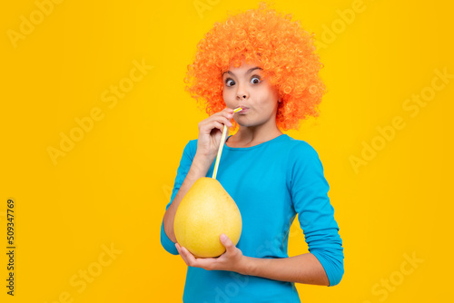 Funny teenage girl hold citrus fruit pummelo or pomelo, big grapefruit isolated on yellow background. Summer fruits. Amazed surprised emotions of young teenager girl.