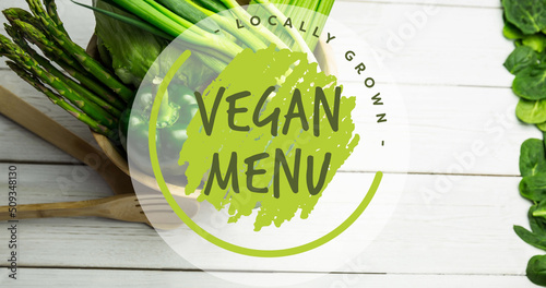 Image of locally grown vegan menu text in green, over bowl of fresh vegetables on white boards