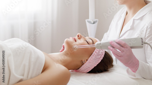 Young woman receiving darsonval procedure electric massage at beauty salon. Hardware cosmetology. photo