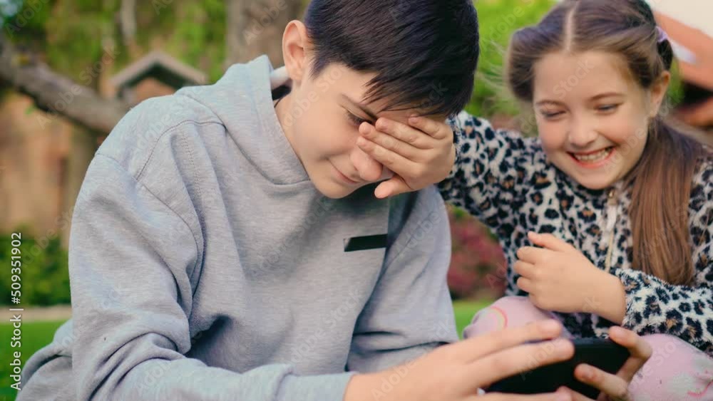 Boy playing on smartphone in mobile games and girl close his eyes with hands and laughing. Concept of digitalization and modern technologies in children environment Boy playing on smartphone in mobile games and girl close his eyes with hands and laughing. Concept of digitalization and modern technologies in children environment