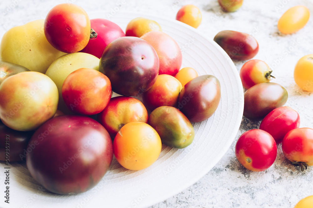 Various colorful tomatoes on white plate on stone table Various colorful tomatoes on white plate on stone table