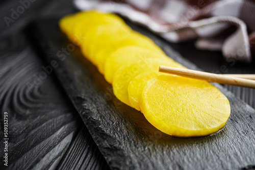 takuan traditional Japanese marinated daikon radish on a dark black rustic wooden background