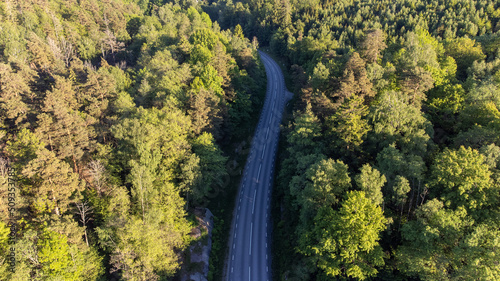 Aerial view of curvy road, lanes with no cars. Drone photography taken from above in Sweden in summer. Surroundings with trees, forest. Travel, transportation concept.