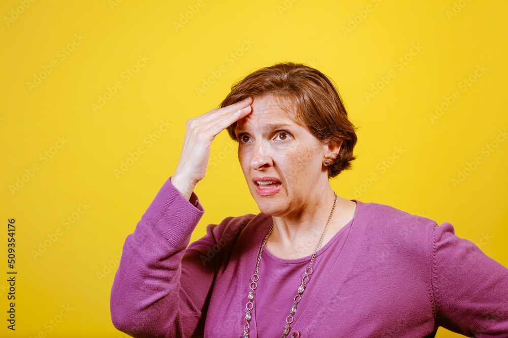 Attractive mature woman in purple blouse on a yellow background with her hands to her head suffering from a headache. Pain Management Concept. Attractive mature woman in purple blouse on a yellow background with her hands to her head suffering from a headache. Pain Management Concept.