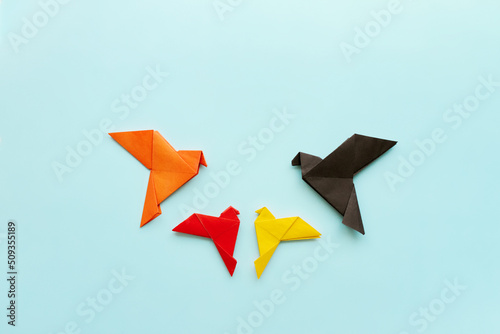 four paper origami pigeons black, orange, red and yellow on light blue background