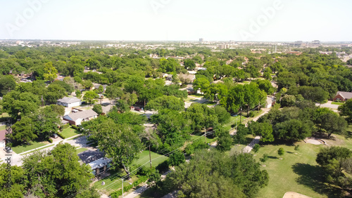 Aerial view typical residential neighborhood surrounded by park and lush green trees with downtown buildings in background in Richardson, Texas, USA