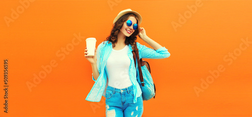 Summer portrait of happy smiling young woman with cup of coffee wearing straw hat, backpack and shirt on orange background, blank copy space for advertising text