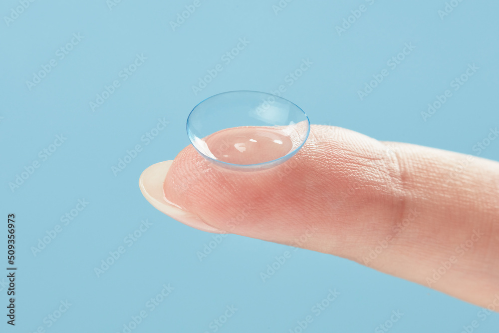 Contact lens on female finger on a blue background, close up. Medicine and vision concept. Woman holding soft contact lens. Shallow depth of field Contact lens on female finger on a blue background, close up. Medicine and vision concept. Woman holding soft contact lens. Shallow depth of field