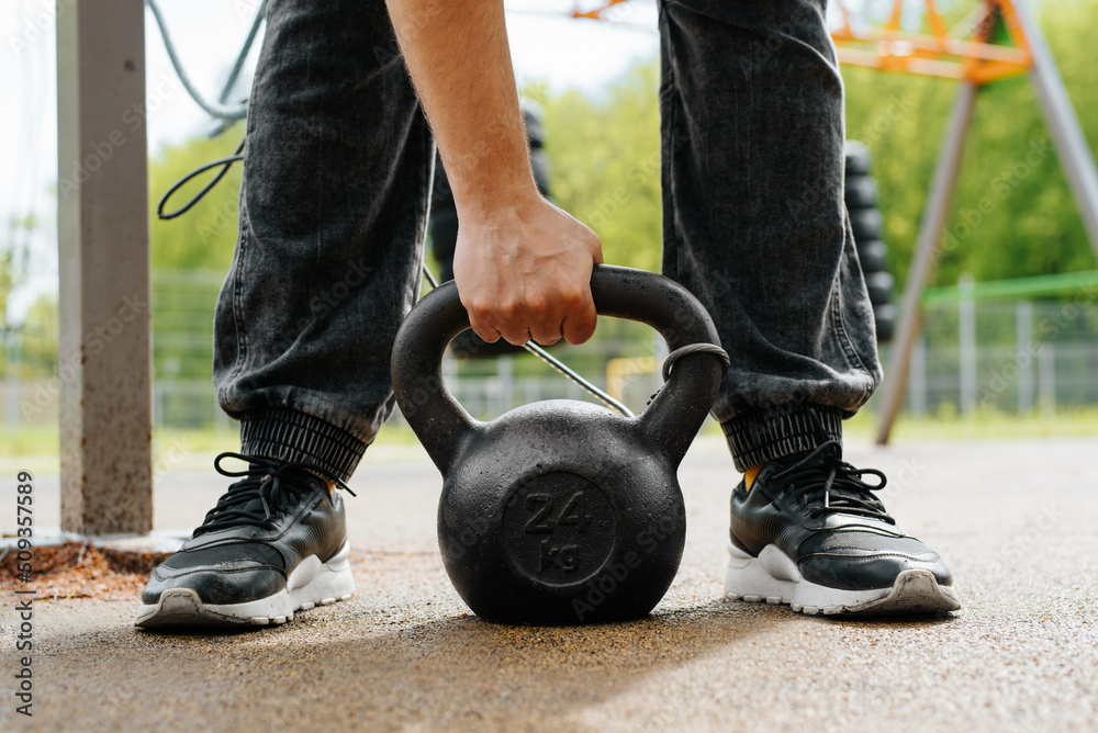 Obraz premium Close-up of a male athlete lifting a heavy weight while standing on a sports field in the park. Weightlifting workout outdoors.