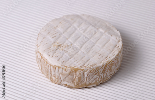 Round Brie cheese with a sections cut out over white corrugated background.