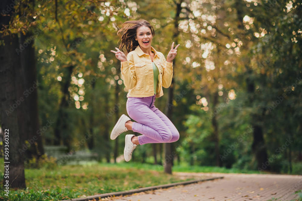 Full length body size view of attractive funky cheerful girl jumping having fun showing v-sign fooling outdoors