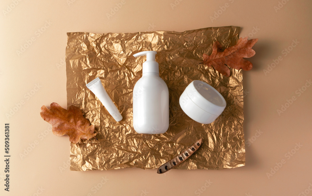 Collection skincare beauty cosmetic products, oak leaves on holidays golden tissue paper on beige Collection skincare beauty cosmetic products, oak leaves on holidays golden tissue paper on beige