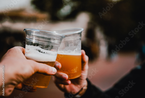 Foto two plastick glass of beer in hand. Beer clinking outdoor