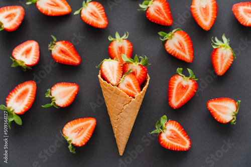 Flat lay with cut strawberries in waffle cone on black background.