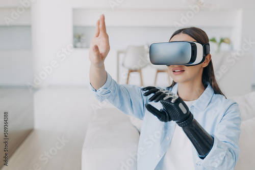 Foto Handicapped girl with cyber bionic hand in virtual reality glasses gets rehabilitation