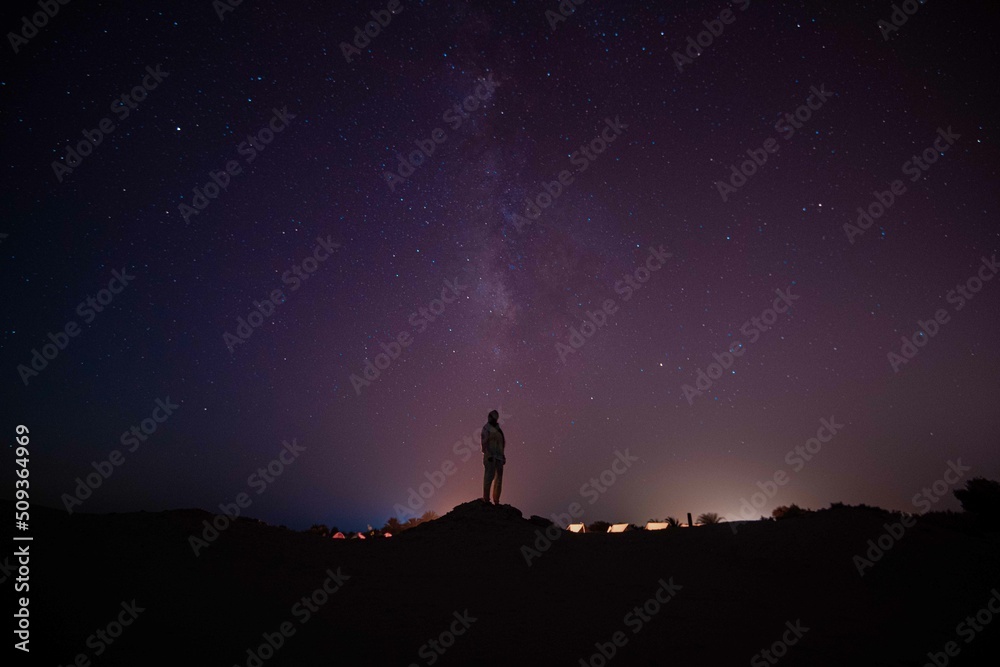 silhouette of a person standing on a rock looking at stars and milky way 